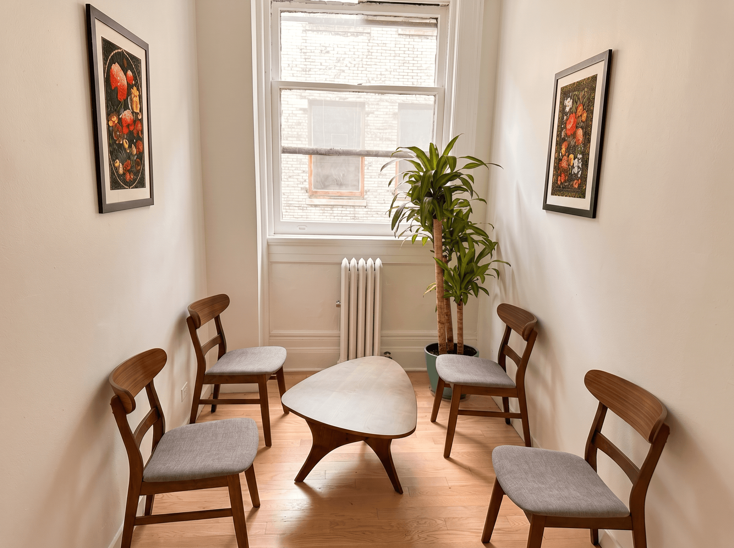 A calm consultation room with wooden chairs around a table, a plant and framed art