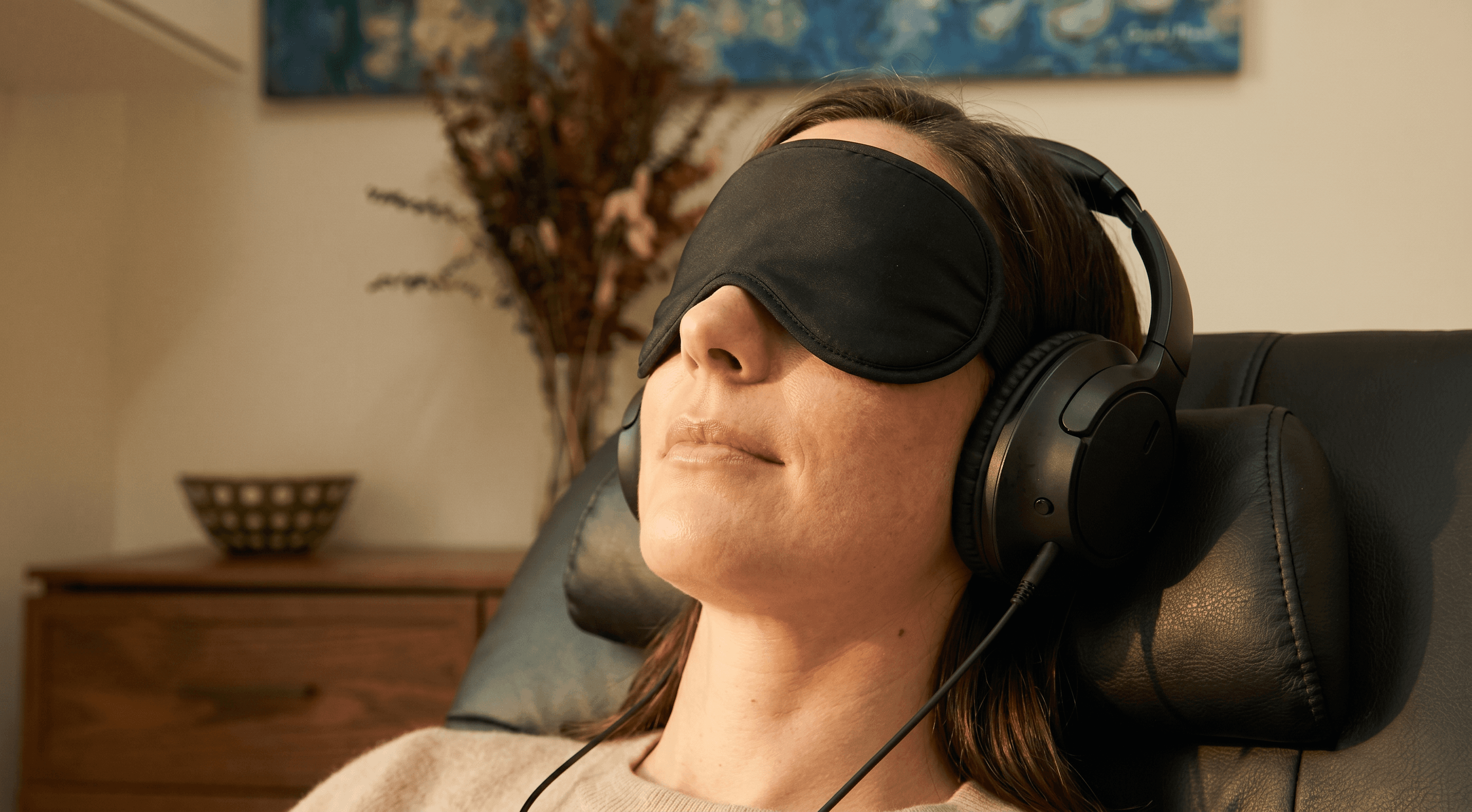 A woman reclining with a black sleep eye-mask and over-ear headphones