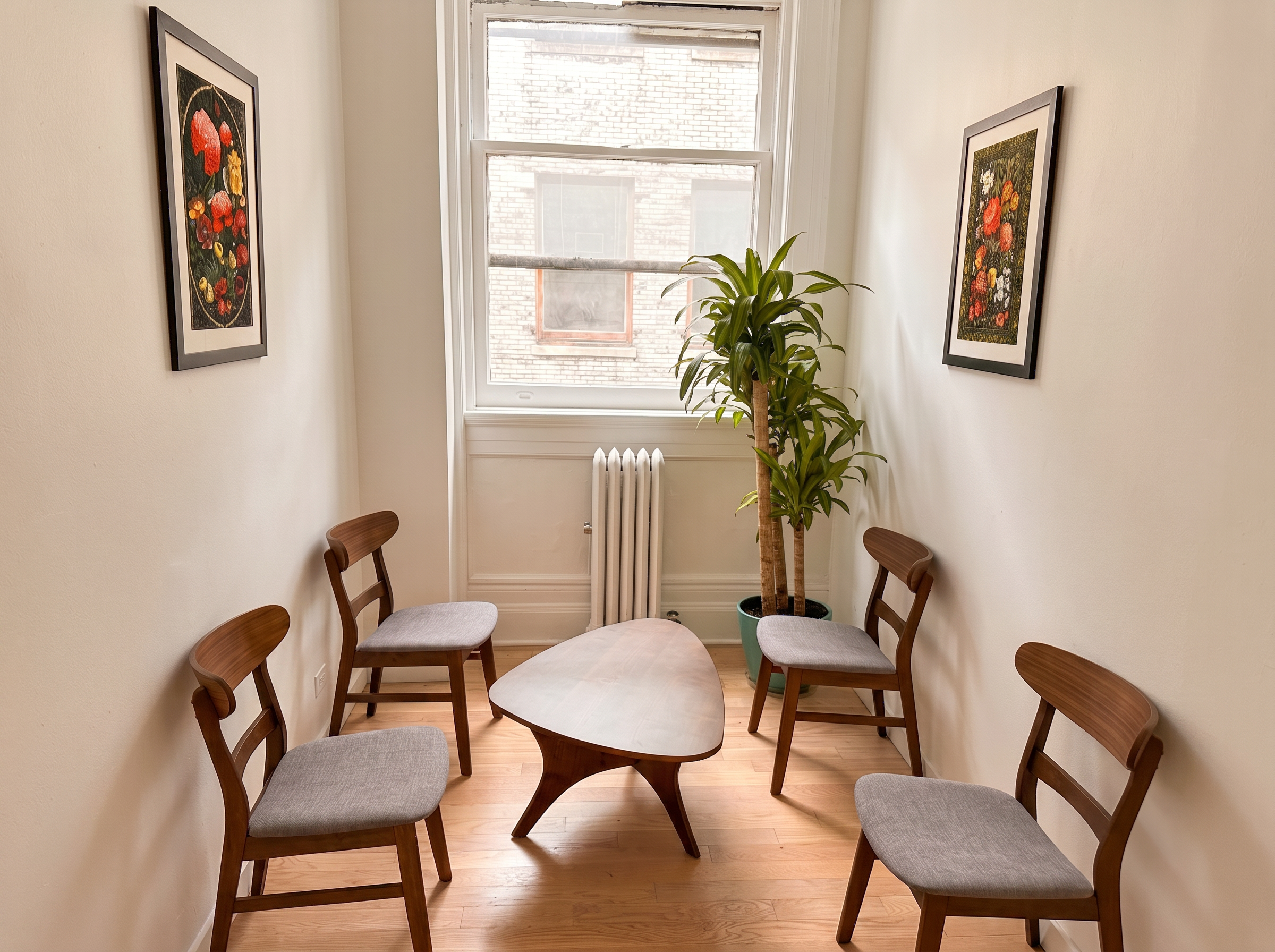 A calm consultation room with wooden chairs around a table, a plant and framed art