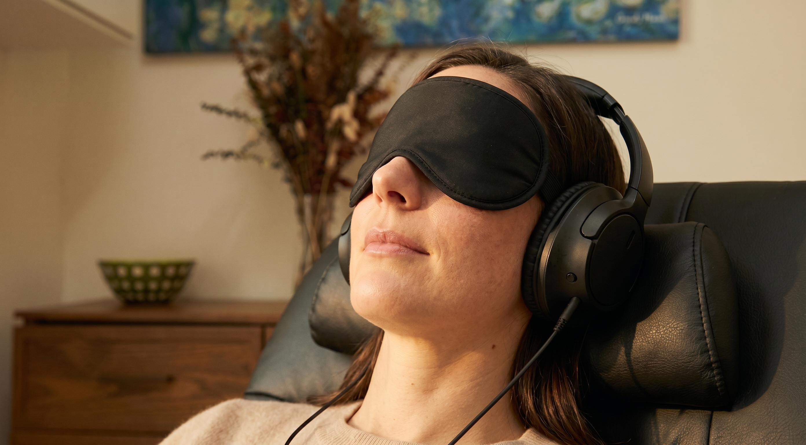 A woman reclining with a black sleep eye-mask and over-ear headphones